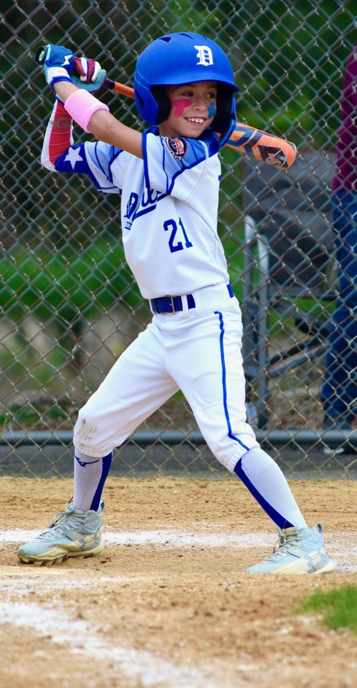A young player at the plate, eye black on, grinning